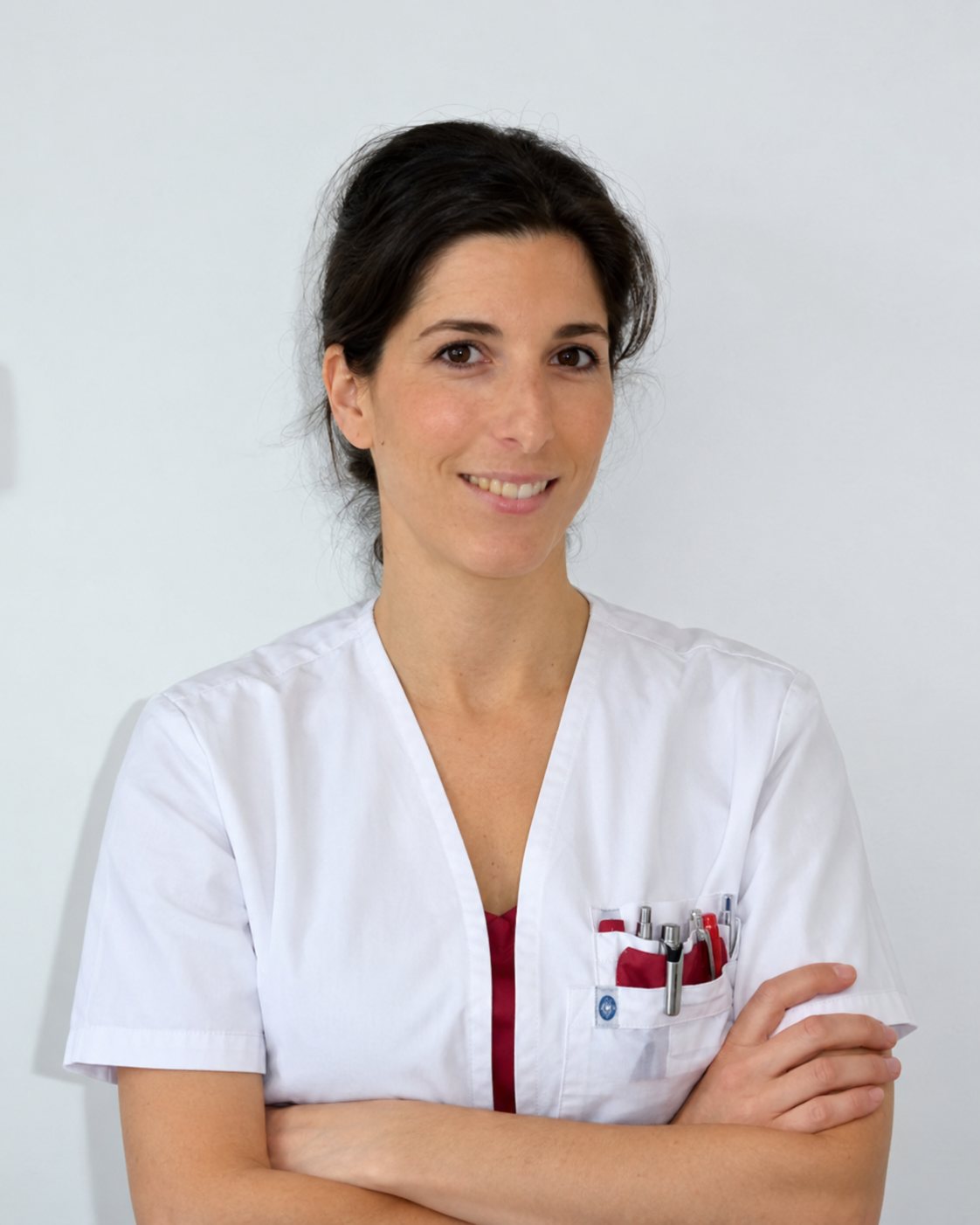 Le Dr Estelle Sebban, cheveux bruns attachés, en blouse blanche, les bras croisés devant un mur clair.