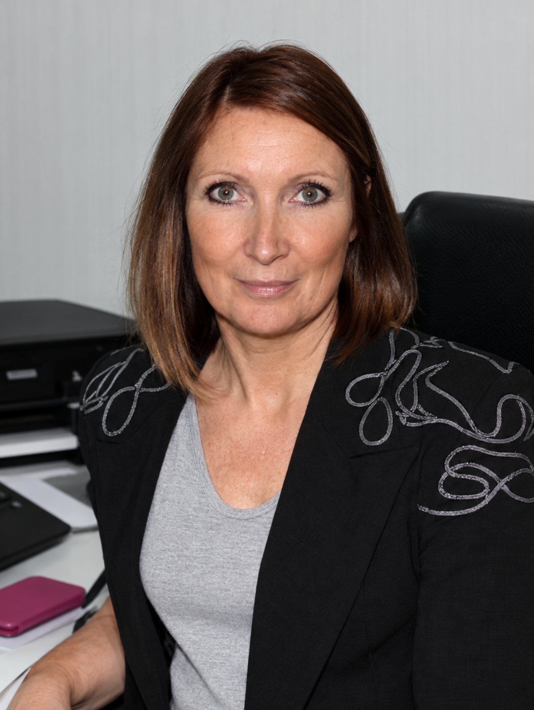 Sylvia, aux longs cheveux bruns, en veste noire, assise dans un bureau devant du matériel informatique.