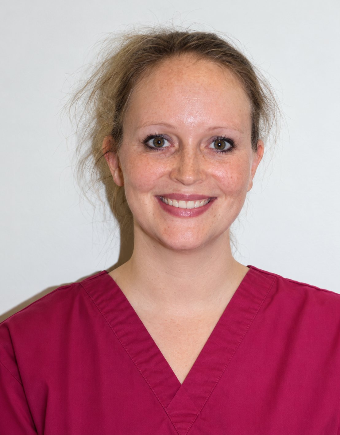 Stéphanie, souriante, cheveux attachés, en tenue médicale bordeaux devant un mur clair.